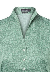 Groene shirt met een draaiend stippenpatroon, een kraag en knoopsluitingen. De stof voelt soepel en licht aan.