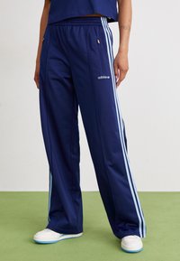 Jūros laivyno treniruočių kelnių modelis su šviesiai mėlynomis šoninėmis juostomis, elastinga juostos ties liemenu, kišenėmis ir "adidas" logotipu kairiajame šlaunyje. Glotni audinio tekstūra.