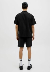 Camisa de manga corta negra y pantalones cortos a juego, hechos de tela texturizada. Llevado con calcetines blancos y zapatos negros. Diseño sencillo, minimalista.
