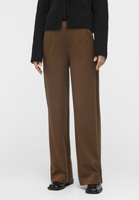 Pantalones de pierna ancha marrones con una textura suave, que cuentan con dos bolsillos laterales y una cintura alta. Combinados con una chaqueta de punto negro texturizada.
