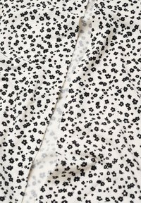 Tissu blanc avec un motif floral noir dispersé. Le matériau présente une texture lisse, avec un léger éclat et des plis subtils.