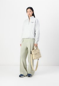 Sweat-shirt à zip gris, pantalon large vert clair, baskets bleues et sac beige avec poches. Tissu doux et coupe décontractée.