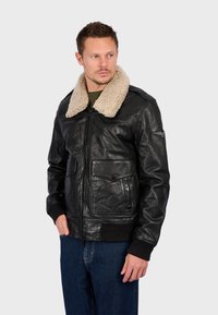 Černá kožená bomber bunda s krémovým ovčím límcem, zipovým zapínáním, dvěma předními kapsami, žebrovanými manžetami a pasem.