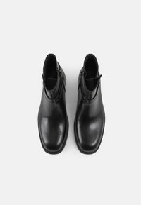 Sorte lær ankle boots med en glat overflade, rund tå og lynlås på siden. Sålen har en let forhøjning. Enkel design.