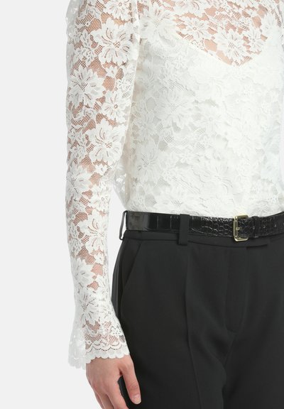 Witte kanten blouse met lange, uitlopende mouwen met bloemenpatroon, gecombineerd met hoog-waist zwarte broek en een glanzende zwarte riem.