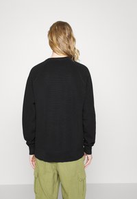 Schwarzer Sweatshirt mit strukturiertem Material, Raglanärmeln und gerippten Bündchen. Getragen mit olivgrünen Cargo-Hosen, die ein lässiges Design zeigen.