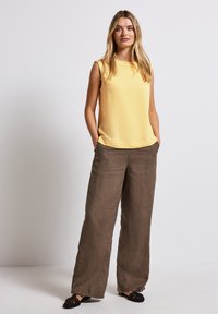 Top giallo senza maniche con una texture liscia, abbinato a pantaloni in lino marroni dalla vestibilità ampia. Entrambi gli indumenti hanno uno stile rilassato e casual.