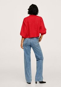 Pull cropped en maille rouge avec des manches larges associé à un jean droit taille haute bleu. Texture lisse et détails minimalistes.