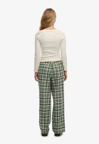 Top de punto crema de manga larga combinado con pantalones verdes de cuadros, holgados. Los pantalones tienen un patrón a cuadros y piernas anchas.