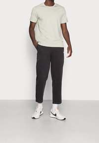 Camiseta de algodón gris claro, pantalones de algodón negros con puños elásticos y zapatillas blancas con detalles negros, combinadas con calcetines blancos de caña corta.