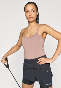 Débardeur marron clair à bretelles fines, associé à un short de sport foncé avec un design superposé et un détail logo.