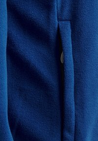 Blå fleece-tyg med en mjuk textur har en sidofliksöppning. Materialet verkar tjockt och varmt, lämpligt för mjuka ytterkläder.