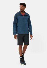 Giacca leggera da uomo in blu scuro, con zip frontale, cappuccio, maniche a contrasto e due tasche laterali, abbinata a pantaloni corti neri e scarpe.