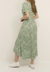 Abito midi floreale verde con maniche corte, caratterizzato da una vestibilità morbida, una texture sottile e un motivo botanico bianco, abbinato a sneakers bianche.