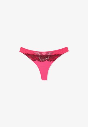 Tanga rosa hecho de un tejido suave, con una cinturilla de encaje en rojo oscuro con bordes festoneados y un diseño semitransparente superpuesto.