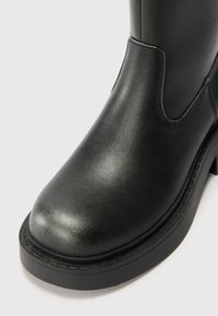 Black leather ankle boot with a rounded toe, flat rubber sole, and elastic side panels. Smooth texture with minimal stitching details.