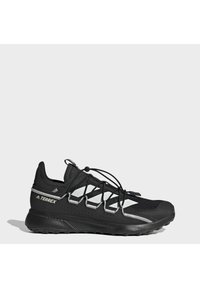 Černá běžecká obuv Adidas Terrex s bílými pruhy, elastickým systémem rychlého šněrování a texturovanou gumovou podrážkou na šedém pozadí.