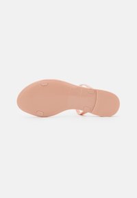 Semelle de sandale rose en caoutchouc texturé, avec une légère courbure et des points de traction circulaires. Branding minimal sur le côté.