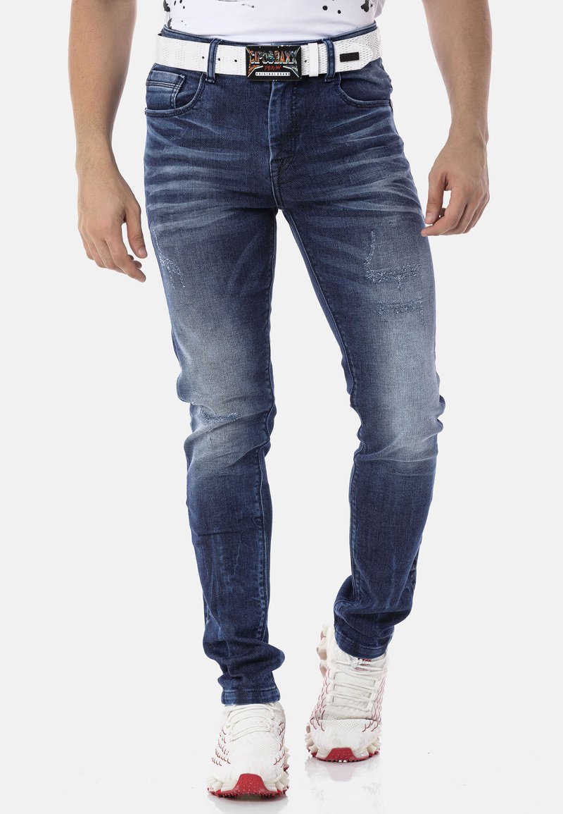 Jean skinny en denim bleu foncé avec un motif délavé. Doté d'une ceinture blanche et de légères déchirures au niveau des cuisses.