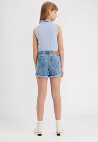Polo sin mangas de color azul claro combinado con pantalones cortos de denim de cintura alta y mangas enrolladas que presentan una etiqueta de parche en la parte posterior y una sutil costura en los bolsillos.