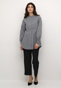 Camicia a righe con vita aderente, maniche lunghe e orlo arrotondato, abbinata a pantaloni neri. Il tessuto ha una consistenza liscia.