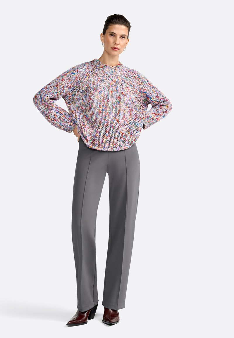 Multikleurige gebreide trui met een ronde halslijn en verlaagde schouders, gecombineerd met grijze slim-fit broek en bordeauxrode hakken.