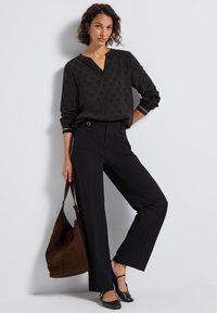 Blouse noire à motifs avec des manches longues ; pantalon noir à jambes larges ; sac à main en daim marron ; chaussures noires avec des brides à la cheville.
