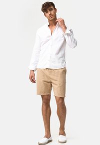 Hvid linned skjorte med knaplukning, beige stribede shorts og hvide slip-on sko. Outfittet kombinerer lette materialer med et afslappet design.