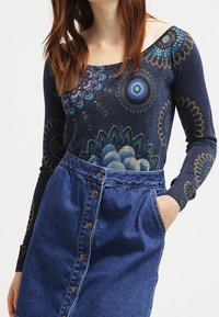 Marineblaues Langarmshirt mit Blumenmuster, kombiniert mit einem hochgeschnittenen Jeansrock, der über Knopfdetails und Seitentaschen verfügt.