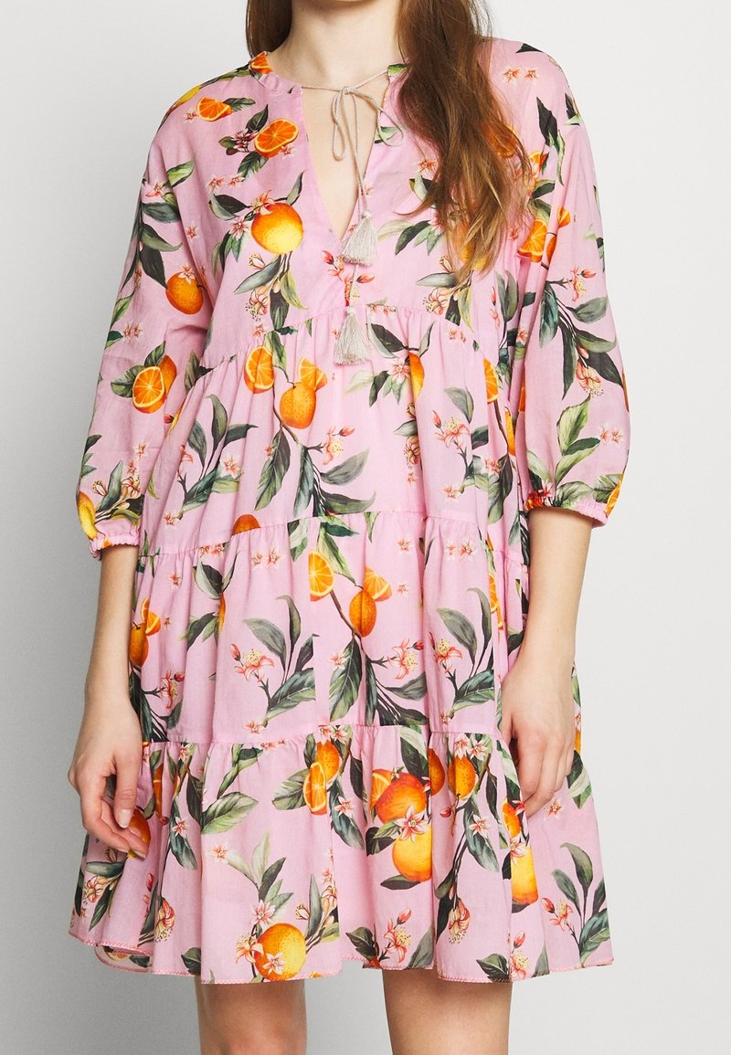 Robe rose à volants avec imprimé de fruits orange et feuilles vertes, manches bouffantes trois-quarts et liens à pompons au col en V.