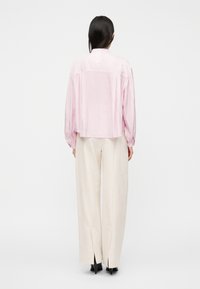 Ροζ ανοιχτόχρωμο πουκάμισο με μακριά μανίκια και κοντό κομμένο σχέδιο, συνδυασμένο με κρεμ παντελόνια με σχίσιμο στα πλαϊνά και μαύρα παπούτσια με ψηλό τακούνι.