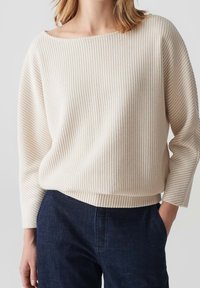 Maglione leggero color crema con righe verticali, scollatura ampia e maniche a tre quarti. Abbinato a pantaloni in denim blu scuro.