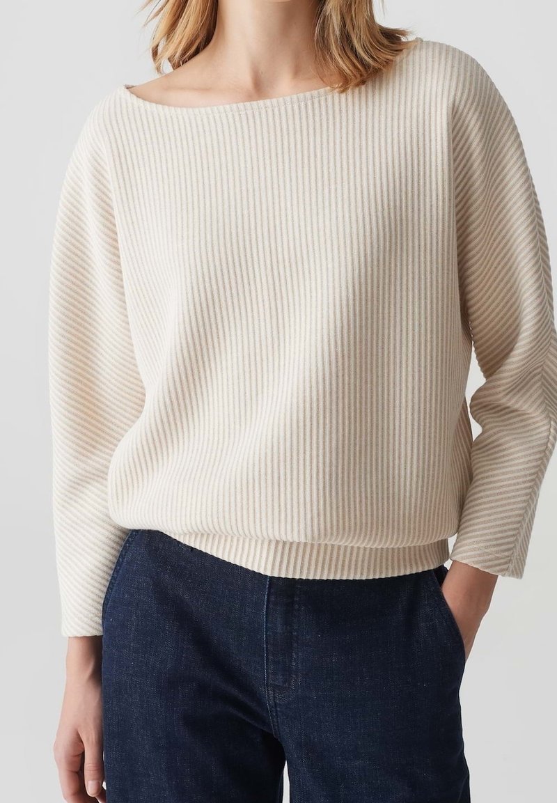 Maglione leggero color crema con righe verticali, scollatura ampia e maniche a tre quarti. Abbinato a pantaloni in denim blu scuro.