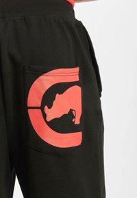 Pantaloni jogger neri con un grande logo di rinoceronte rosso sulla tasca posteriore. Tessuto morbido con vita a coste e tasche laterali.