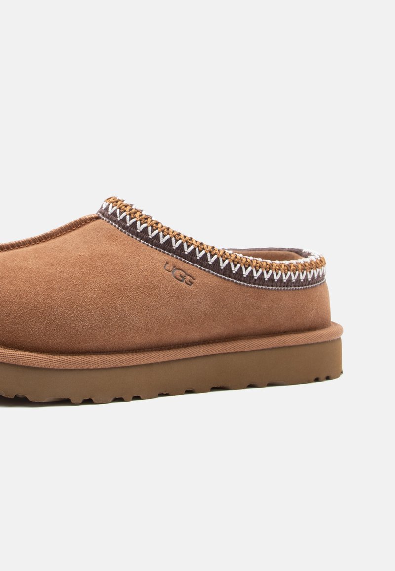Chaussure slip-on en daim marron avec couture décorative le long du col, semelle en caoutchouc et logo UGG sur le côté.