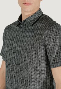 Camicia a maniche corte con bottoni in bianco e nero, caratterizzata da un motivo geometrico, colletto e tessuto leggero.