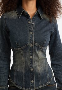 Donkerblauwe denim overhemd met een getailleerd ontwerp, spitse kraag en contrasterende zilveren knopen aan de voorkant. Merkbare vervaging op de stof.