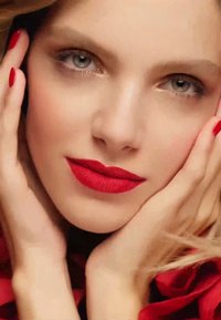 Närbild av ett ansikte med felfri hy, djärva röda läppar och manikyrerade röda naglar. Bakgrunden har mjukt, flödande tyg i rött.