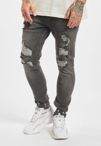 Slim-fit grå jeans med ødelagte rifter og frynsete kanter. Kombinert med hvite joggesko for et avslappet utseende.
