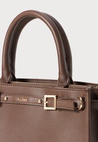 Sac à main en cuir marron avec une texture grainée, deux poignées rondes, des détails en métal doré et une fermeture éclair. Logo ALDO présent à l'avant.