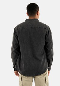 Camisa de mezclilla gris oscuro con mangas largas, cuello clásico y dobladillo curvado. La vista posterior muestra detalles de costura y puños abotonados.