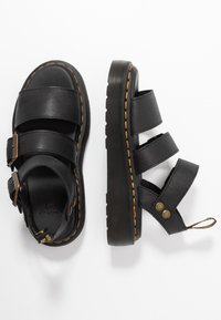 Zwarte leren sandalen met drie brede banden en een verhoogde zool. Heeft contrasterende gele stiksels en metalen hardware accenten.