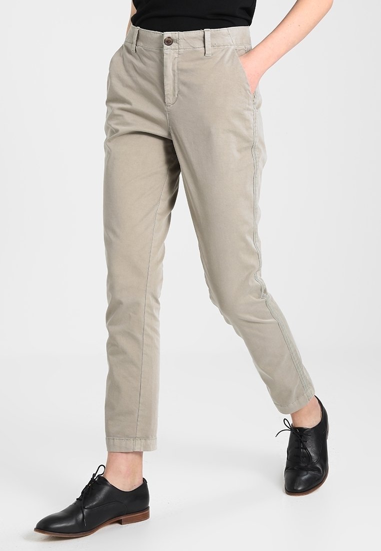 Chino beige chiaro con gamba affusolata, tasche frontali, chiusura con bottone singolo e dettagli cuciti, abbinati a scarpe oxford nere.
