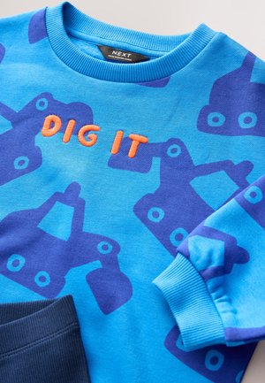 Felpa blu con un audace motivo di veicoli da costruzione blu e viola. Ricamo arancione con la scritta "DIG IT" sul davanti, polsini a costine.
