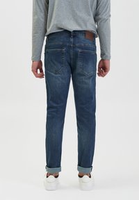 Męskie ciemnoniebieskie dżinsy, slim fit, z brązową skórzaną naszywką na tylnej części w pasie, podwinięte mankiety i klasyczny design kieszeni.