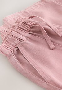 Pinke Jeanshose mit elastischem Bund und Kordelzug, zeigt Vordertasche und detaillierte Nähte auf hellem Hintergrund.