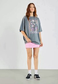 Šedé oversized tričko s květinovou grafikou a textem "KVĚTINY", doplněné o růžovou mini sukni. Černé tenisky a bílé kotníkové ponožky dotvářejí celkový vzhled.