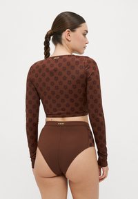 Braunes langärmliges Cropped-Top mit einem dunklen Blumenmuster und goldenen Logodetails; passende hochtaillierte Unterteile in einfarbigem Braun mit glatter Textur.