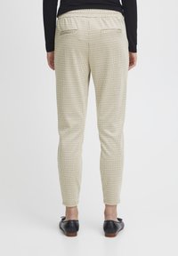 Beige checkered trousers with a fitted silhouette, elastic waistband, and two back pockets, paired with black loafers.