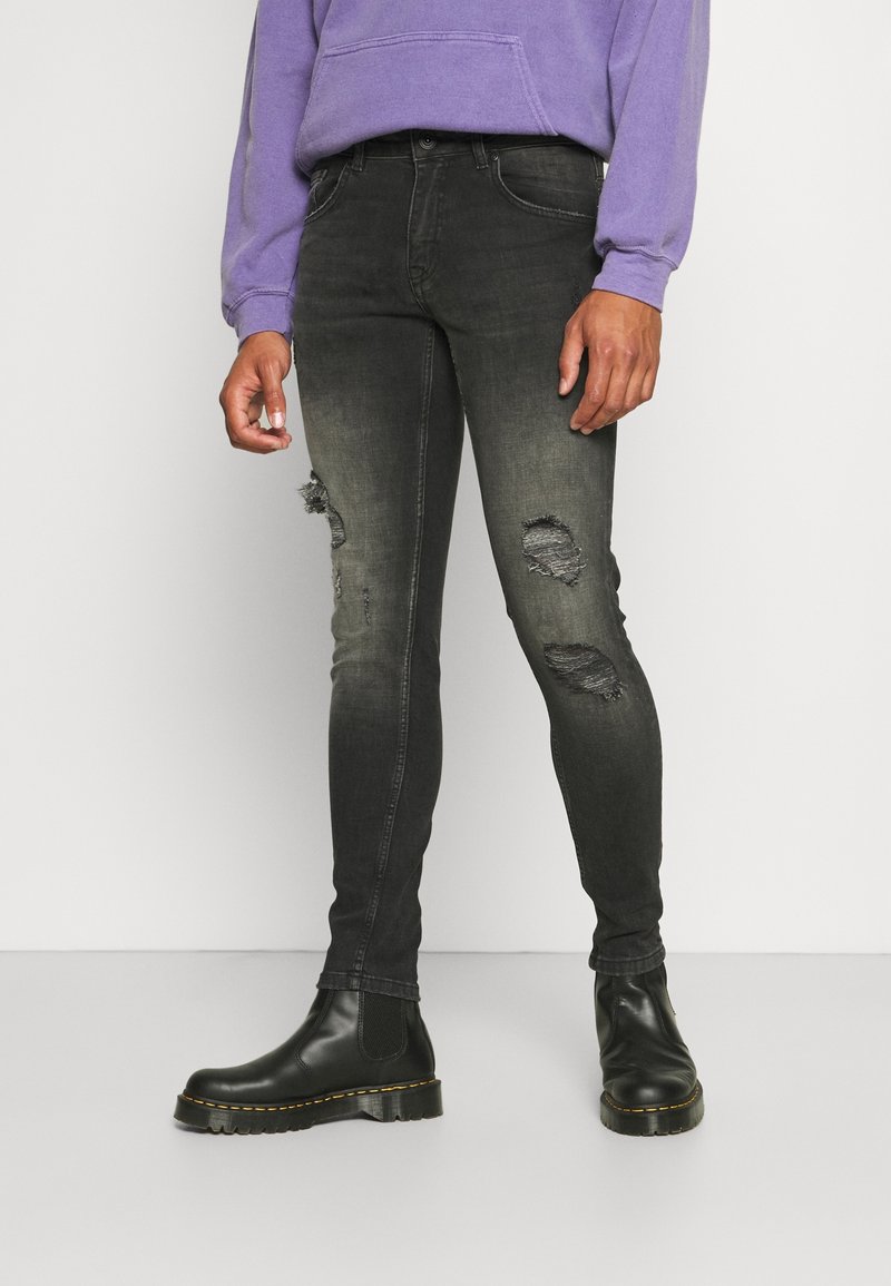 Jeans ajustados de mezclilla negra con detalles desgastados, combinados con botas chelsea negras. El modelo lleva una sudadera morada. Textura suave y corte ajustado.